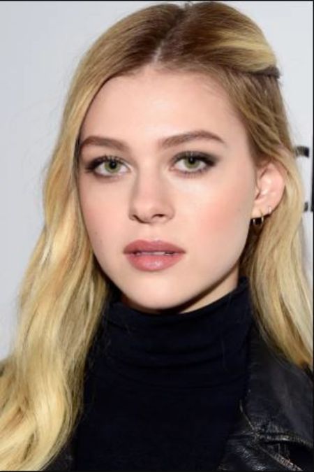 Nicola Peltz in a black sweater and jacket poses for a picture.